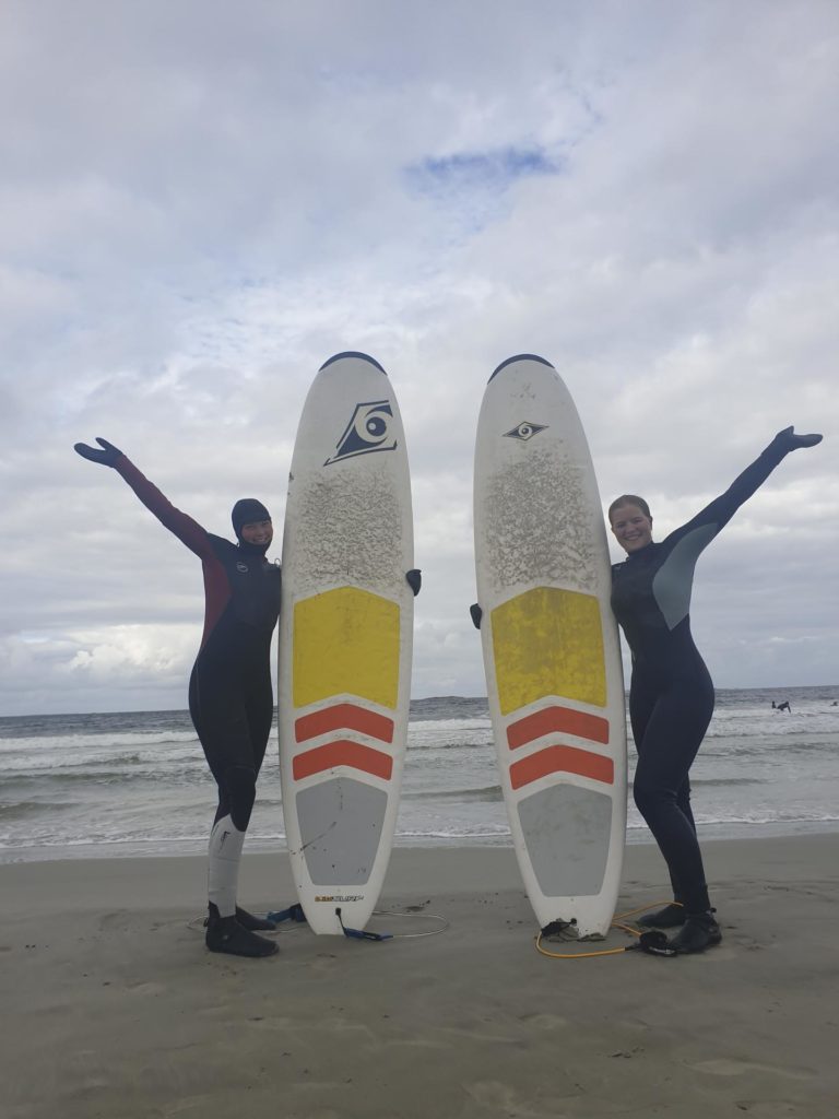 Two people posing with surfboards on the beach