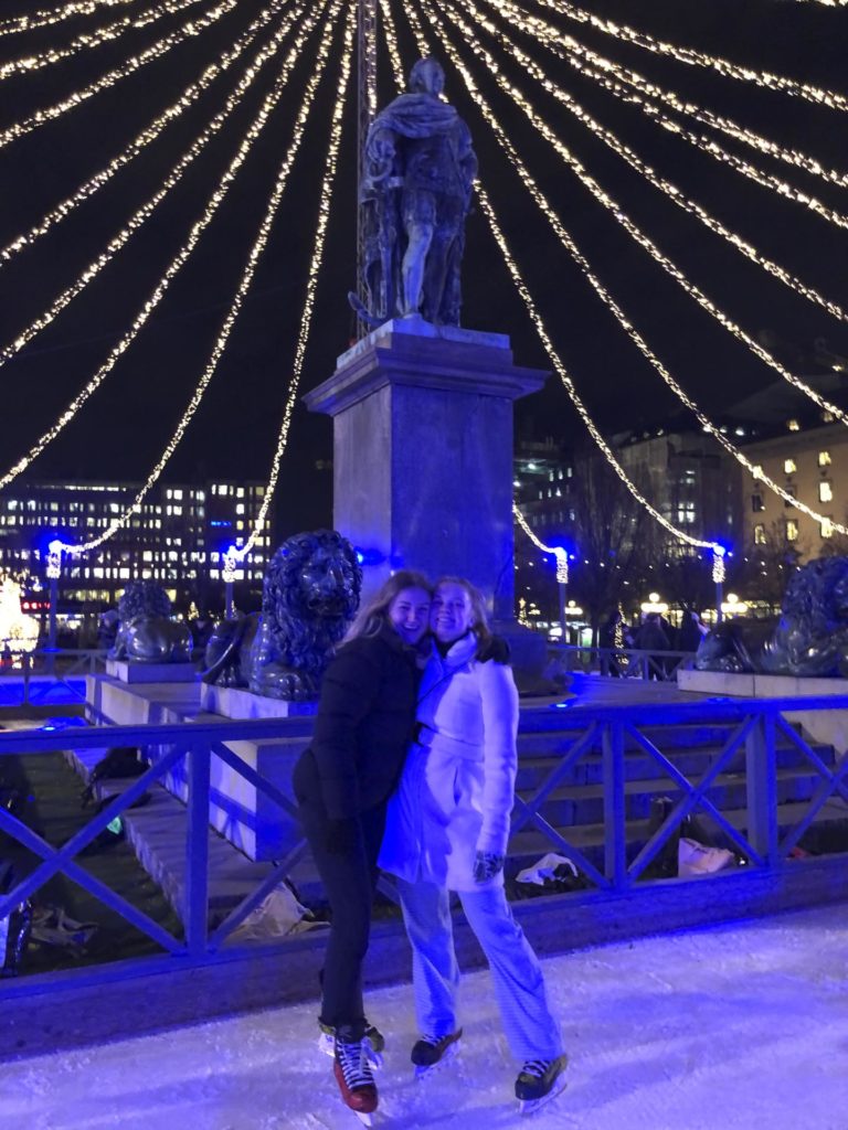 To unge kvinner poserer foran en skulptur med julebelysning