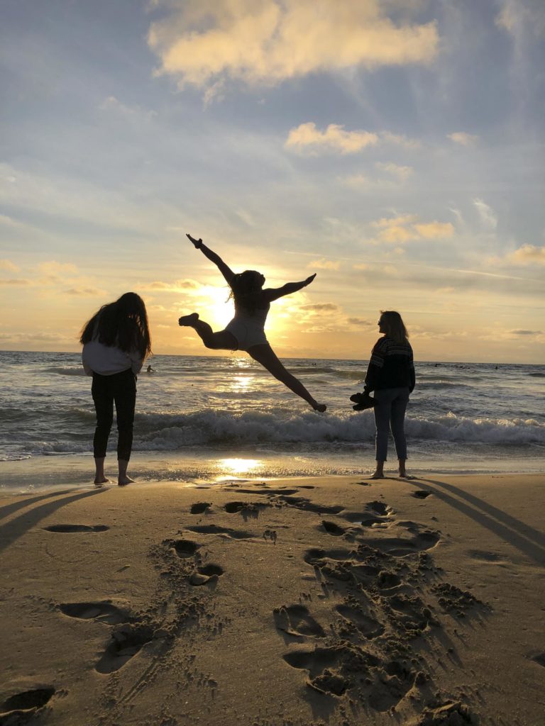 Silhuetter av unge mennekser hopper på stranda i solnedgang