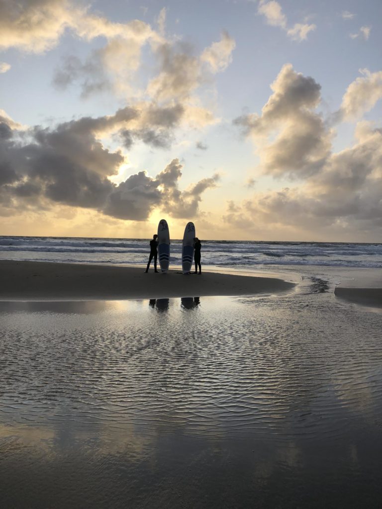 Silhuetter med surfebrett på en strand i solnedgang