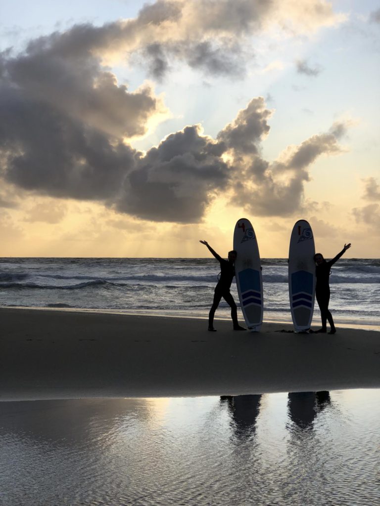 Silhuetter med surfebrett på en strand i solnedgang