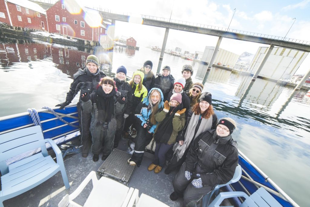 Smiling young people in the bow of a fishing boat drive into Svolvær