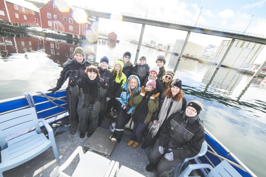 Smilende unge mennesker i baugen på en fiskebåt kjører inn i Svolvær