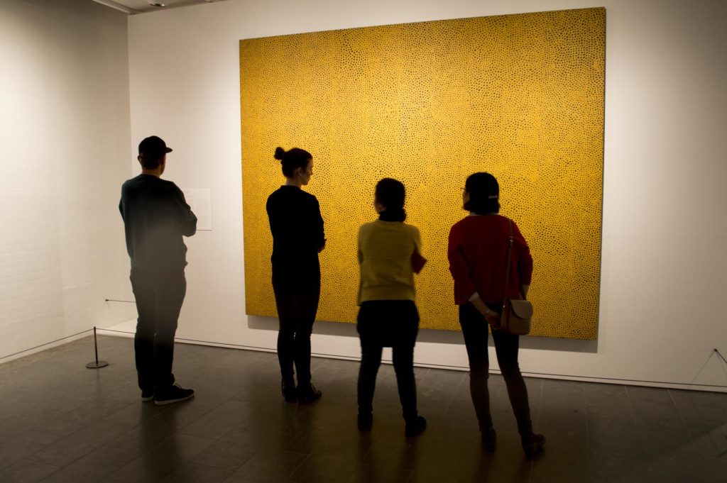 Mennesker studerer et stort gult bilde i et galleri