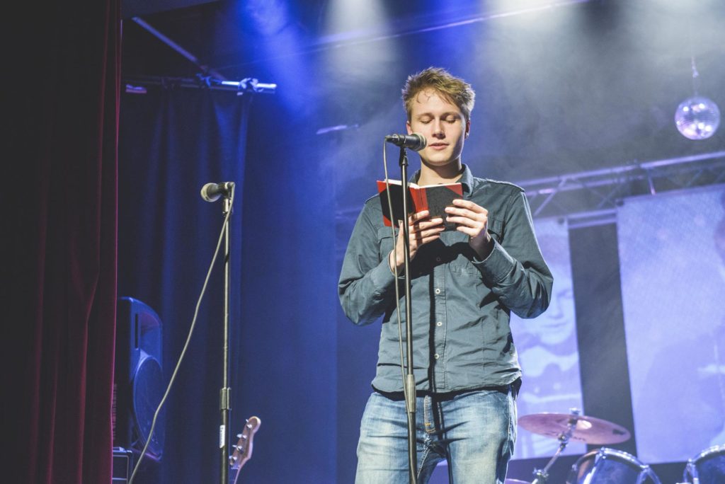 Young man reading poems on stage