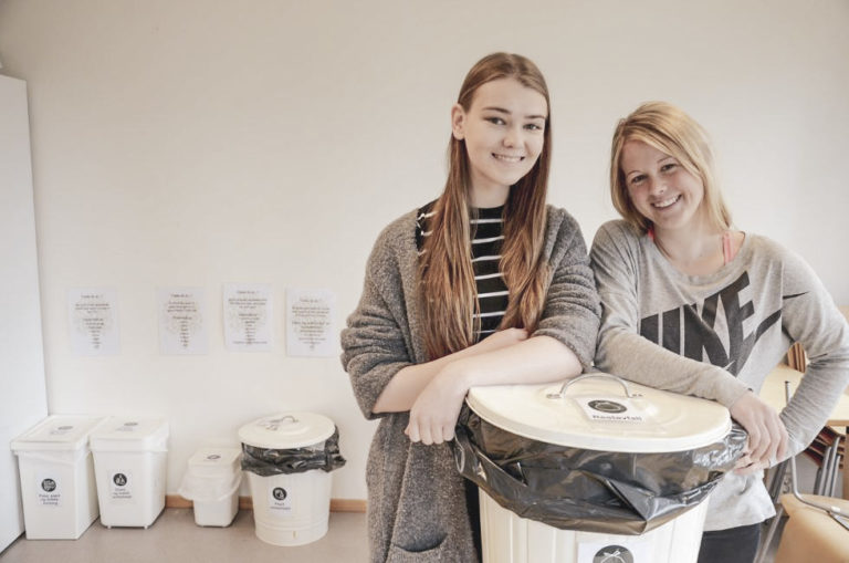 To unge kvinner poserer med en søppelbøtte